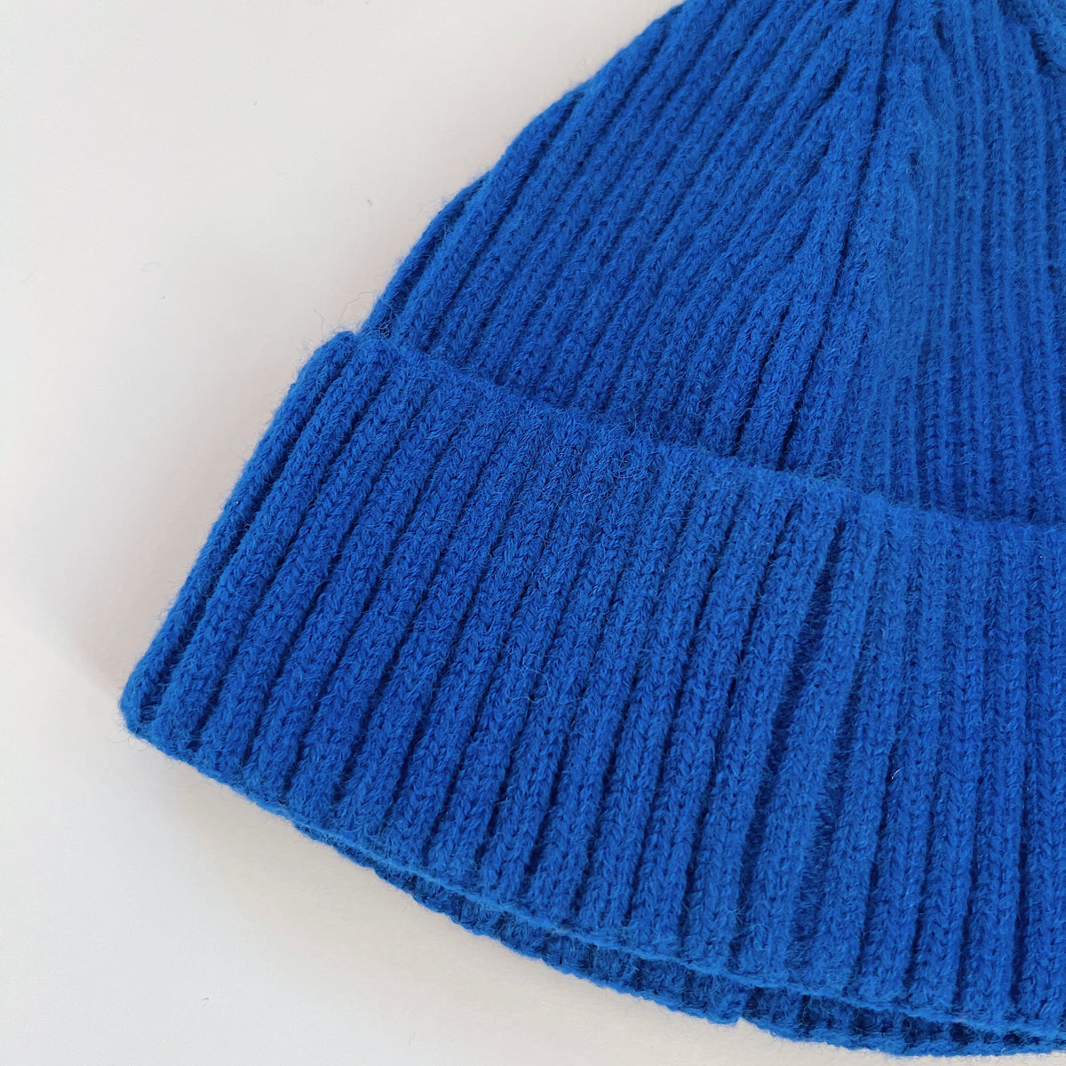 Close-up of the cobalt blue lambswool beanie showing its ribbed knit texture and folded cuff.
