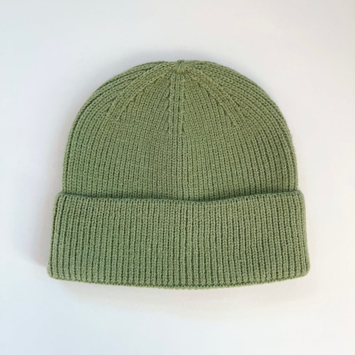 Pistachio green lambswool beanie laid flat with a rounded knit crown and ribbed fold-over cuff.

