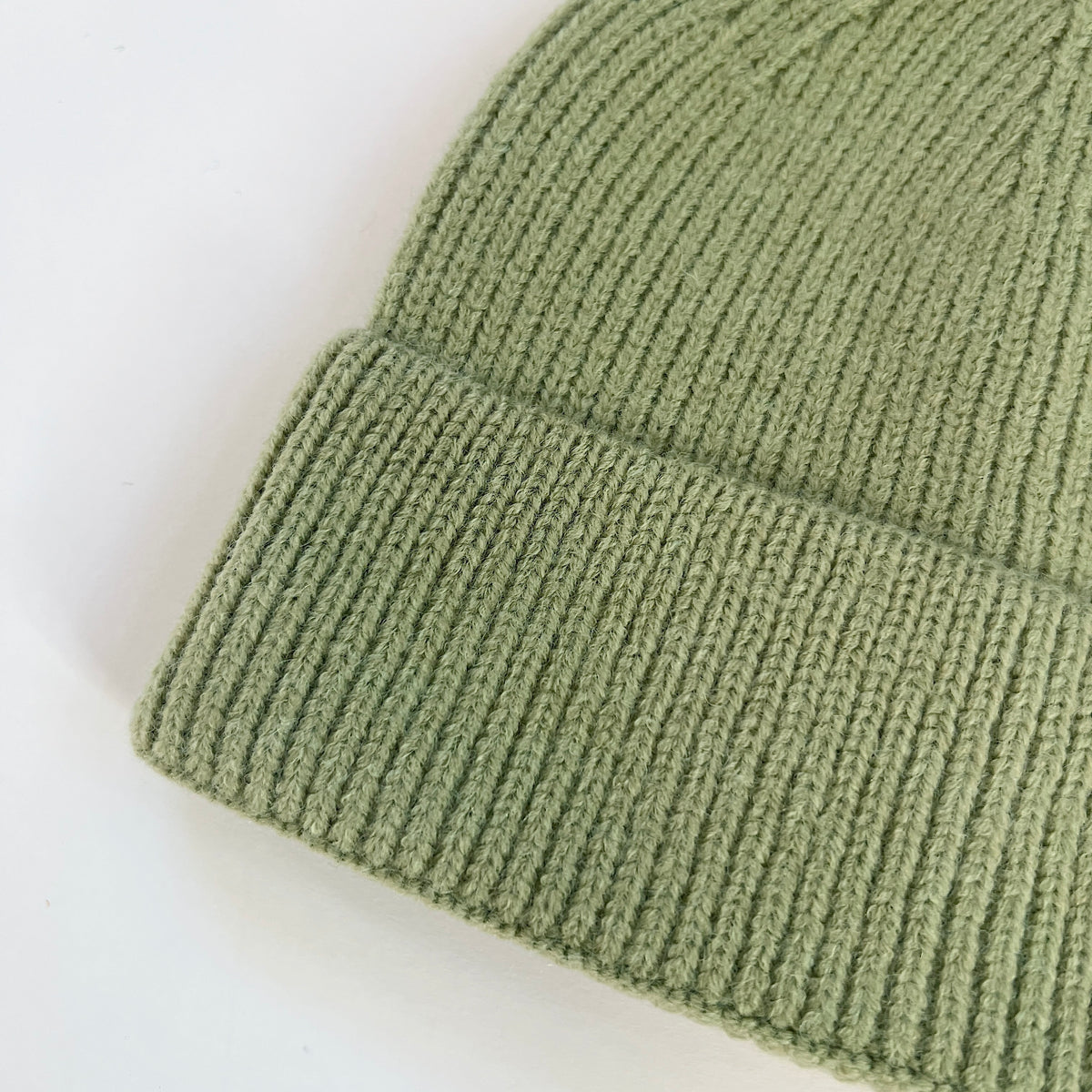 Close-up of the pistachio green lambswool beanie showing its knit texture and ribbed folded cuff.
