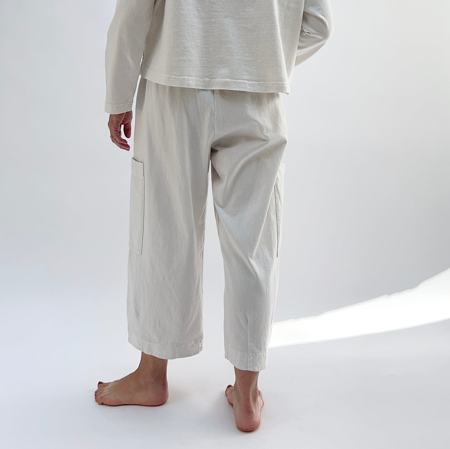 A person standing in a studio setting, wearing cream-colored cotton pants with a wide fit and high waist, paired with a matching top.