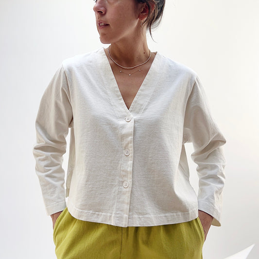 A woman wearing a beige button front crop cardigan with long sleeves and a V-neck, paired with green pants.