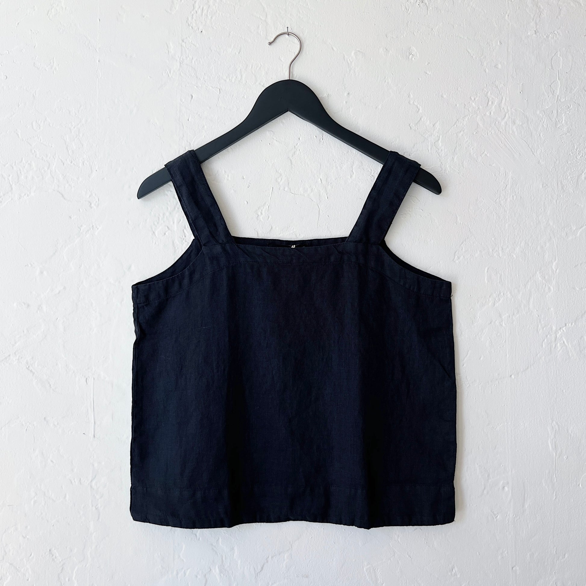 A square neck linen tank in black, hanging on a hanger against a white wall.