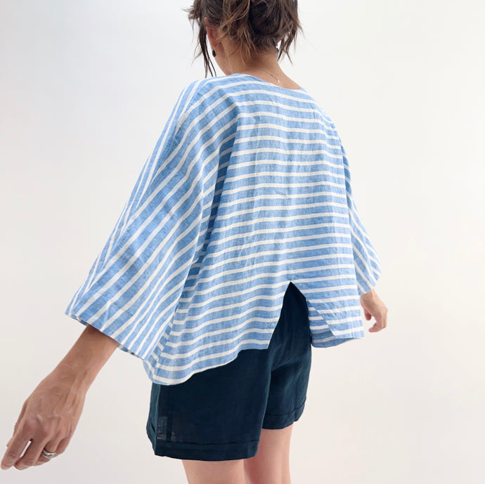 Person wearing a blue and white striped shirt and dark shorts on a plain background