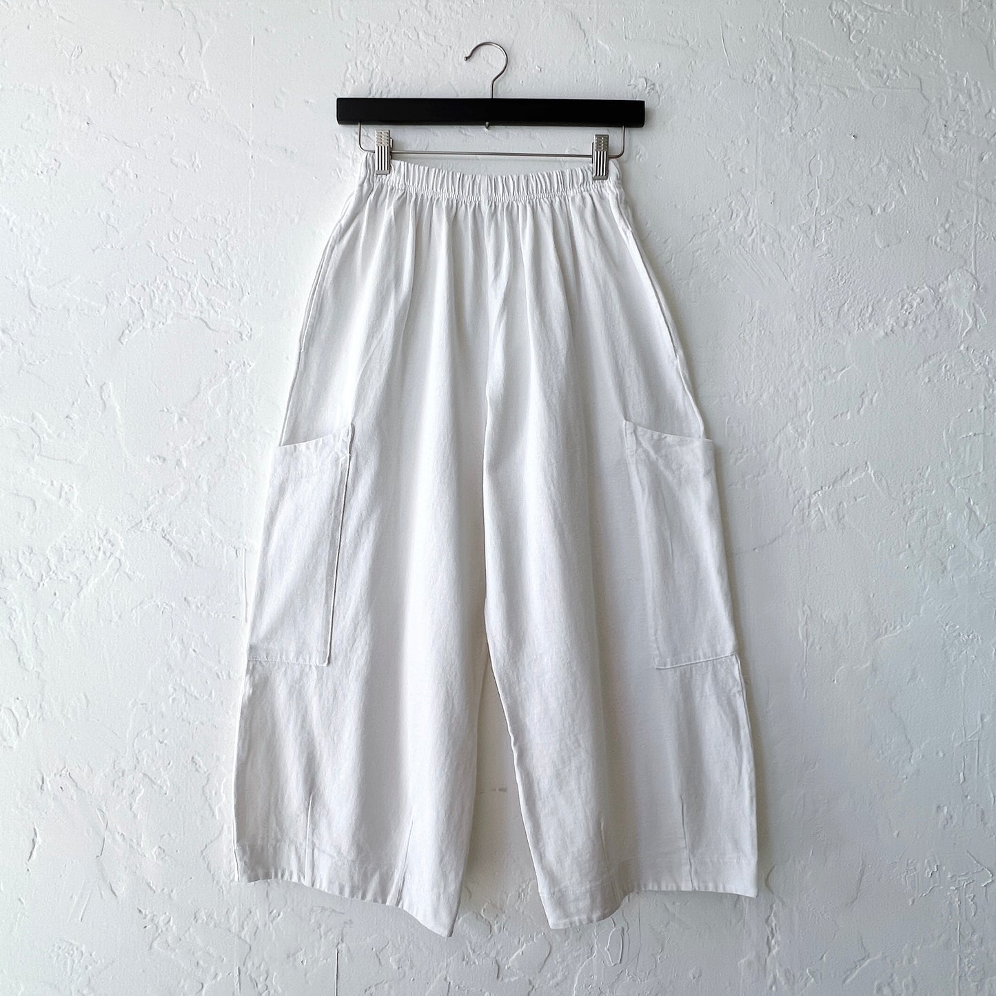 White wide-leg pants on a hanger against a white wall