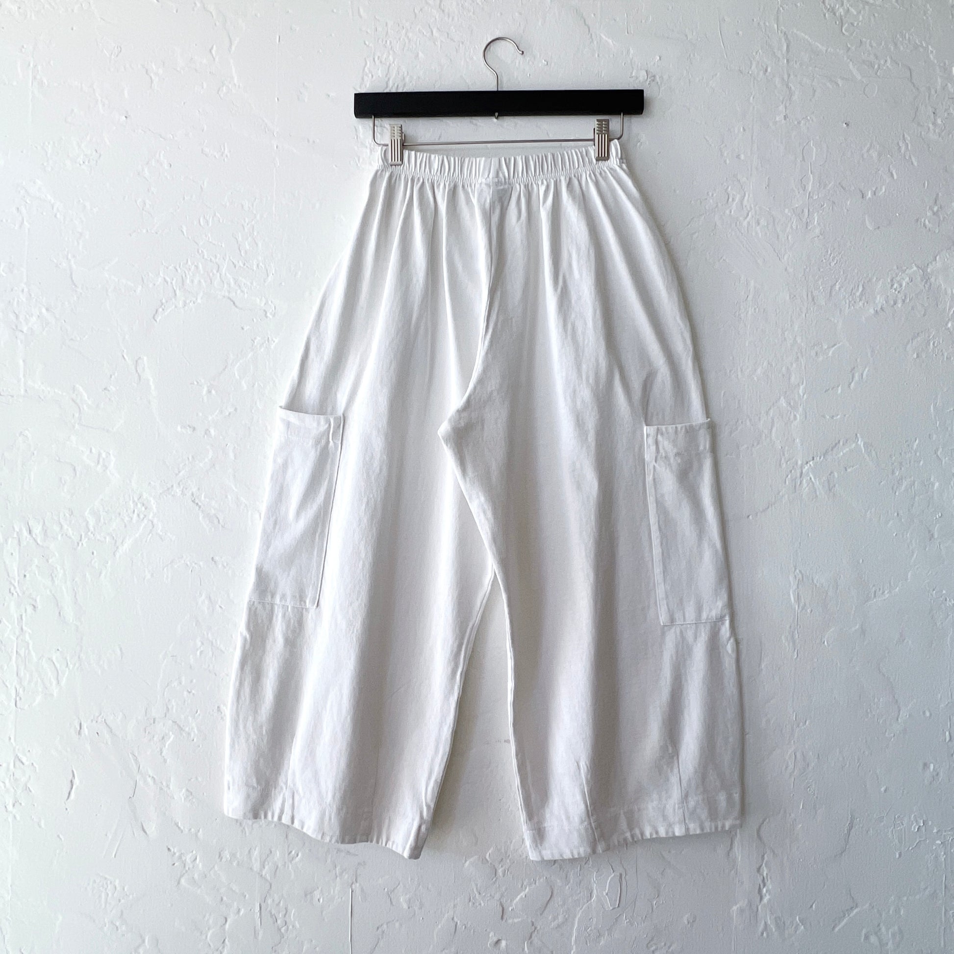 White pants hanging on a hanger against a white wall
