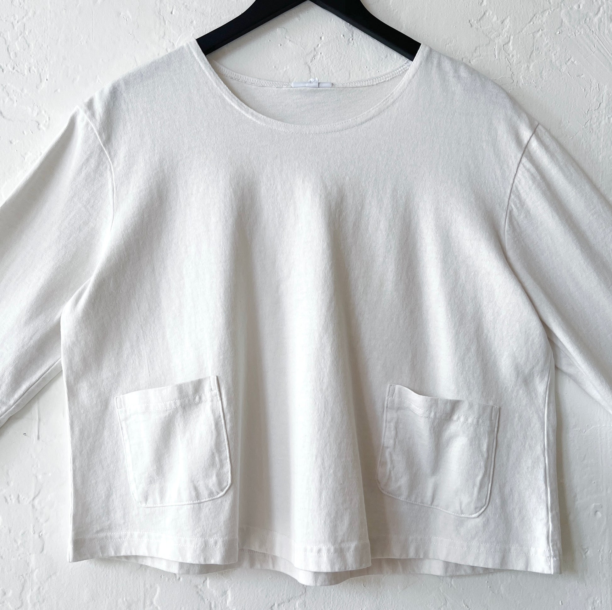 White shirt with two front pockets on a hanger against a white background