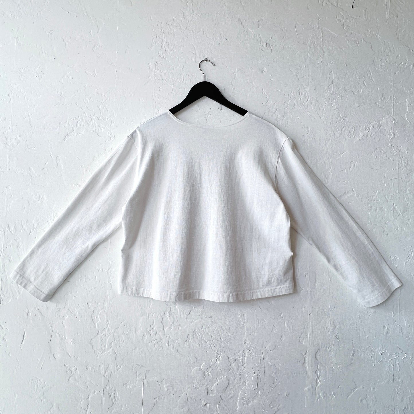 White long-sleeve shirt on a hanger against a white wall