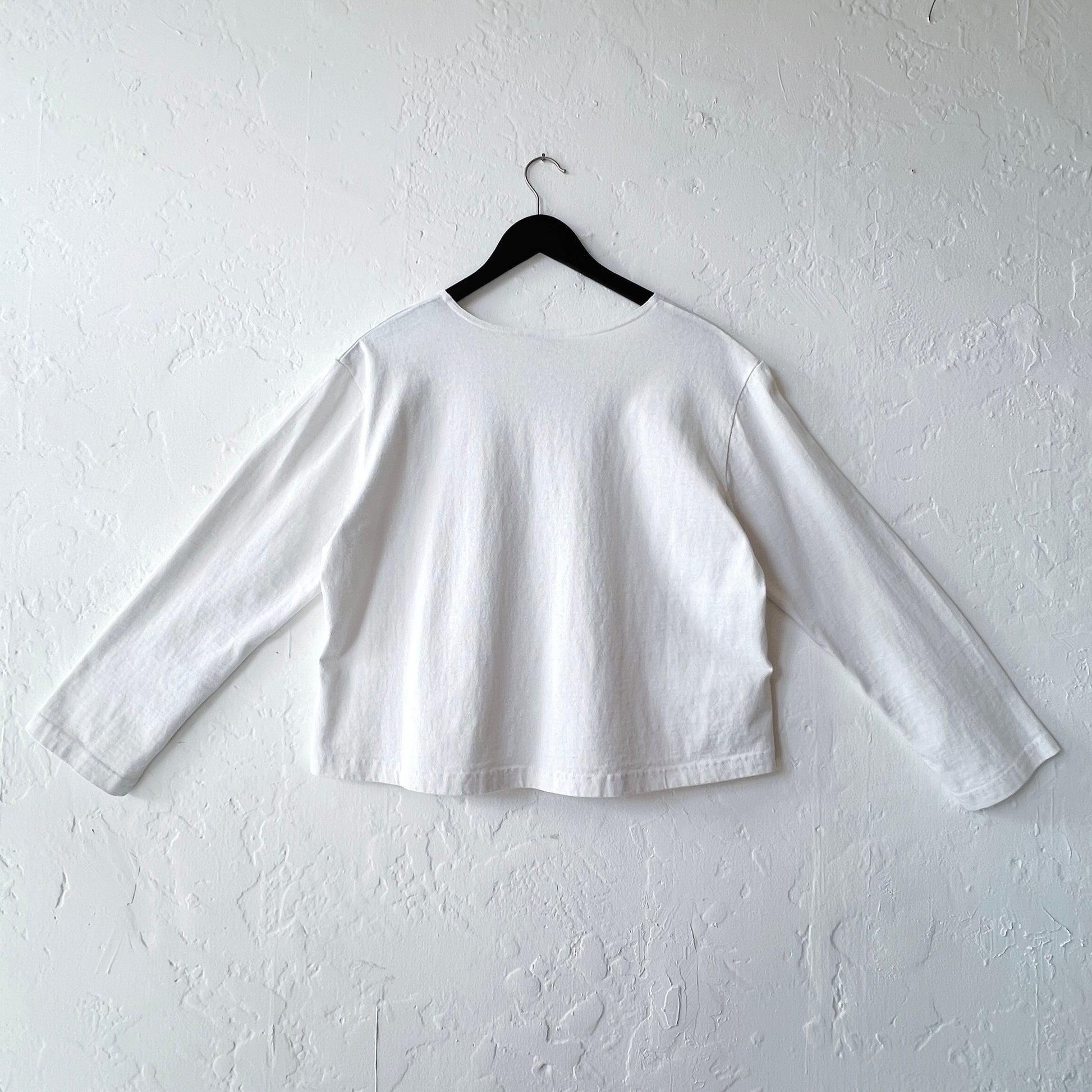 White long-sleeve shirt on a hanger against a white wall