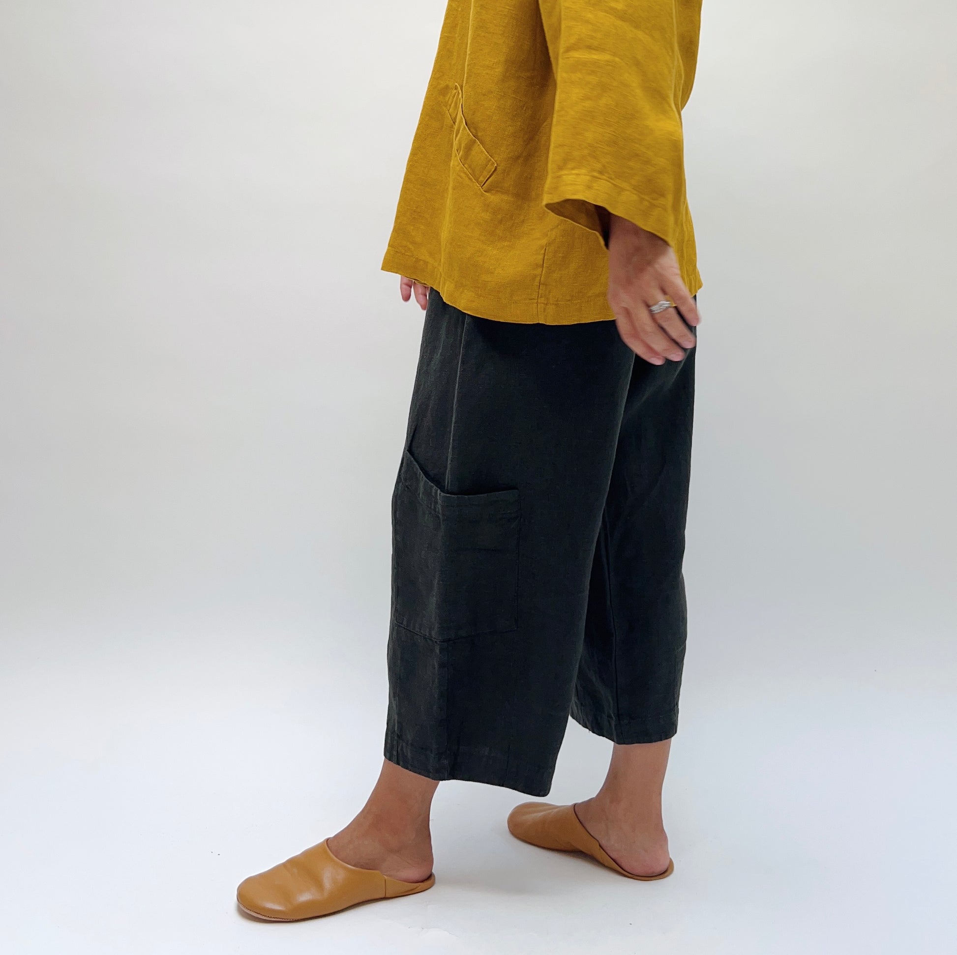 Side view of Bryn Walker Heavy Linen Casbah Pant in black, showing wide-leg silhouette and patch pocket at hip, styled with a mustard linen top and tan leather mules

