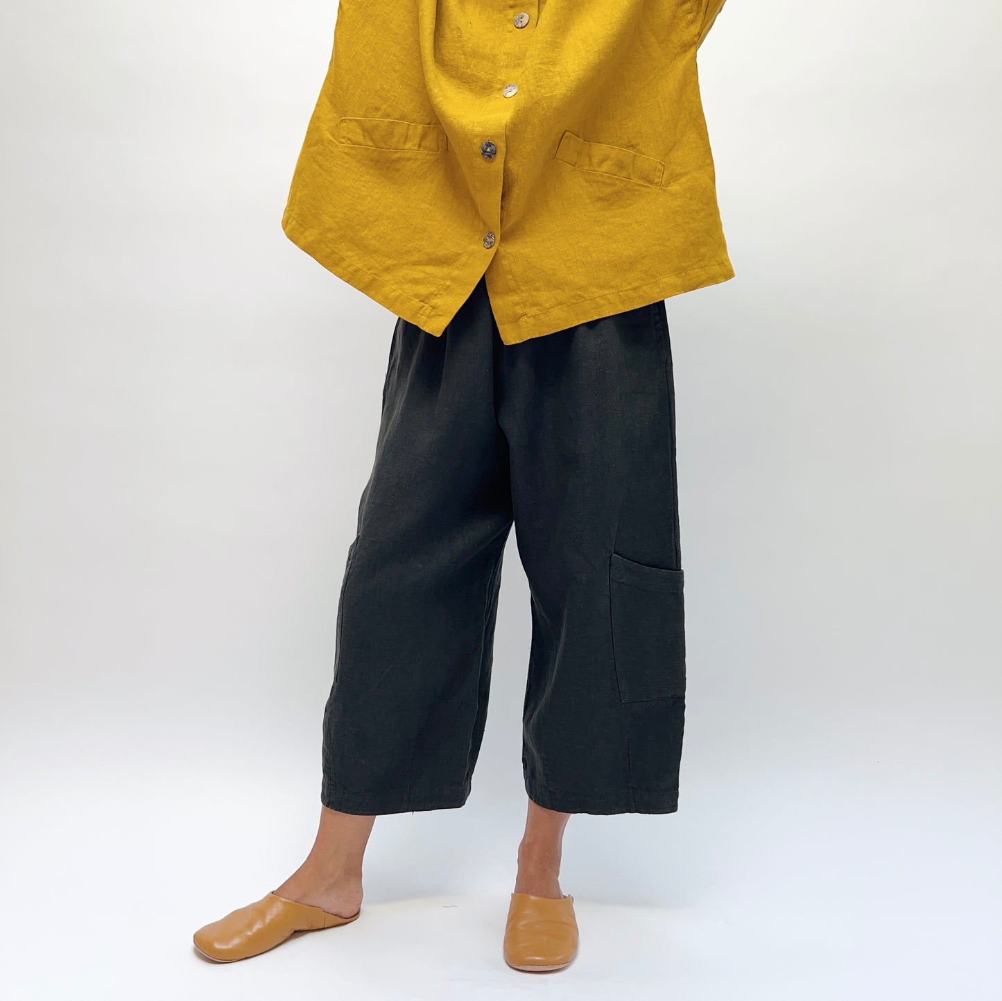 Front three-quarter view of Bryn Walker Heavy Linen Casbah Pant in black, showing relaxed wide-leg fit and patch pocket detail, styled with a mustard linen jacket