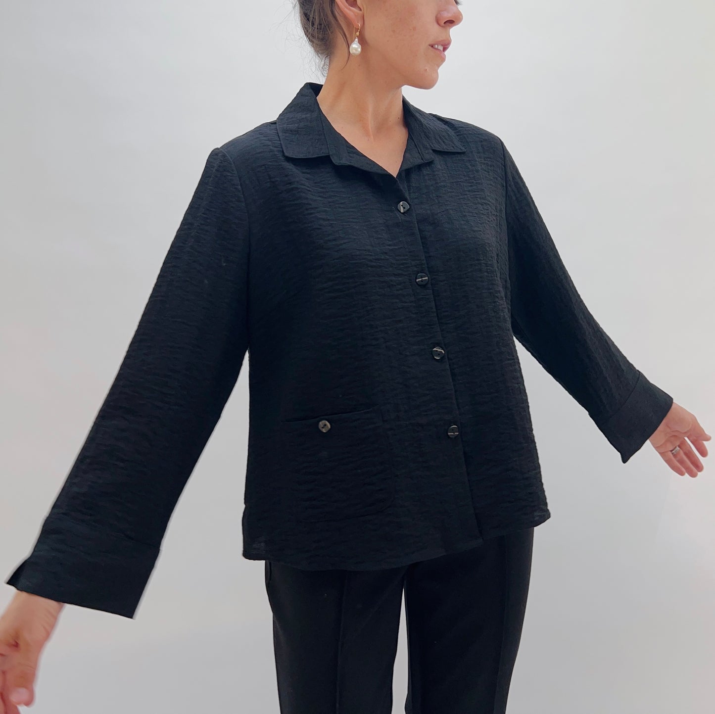 Person wearing a black textured jacket and pants against a white background