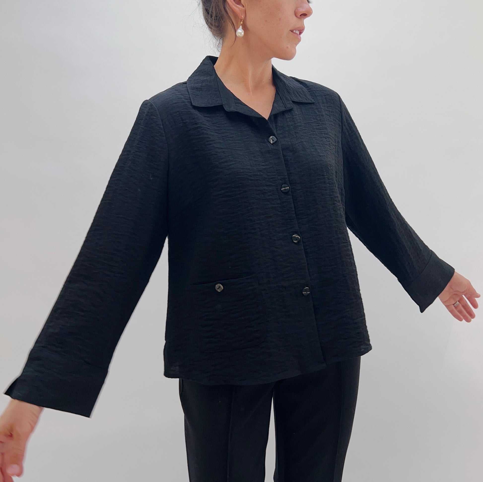 Person wearing a black textured jacket and pants against a white background