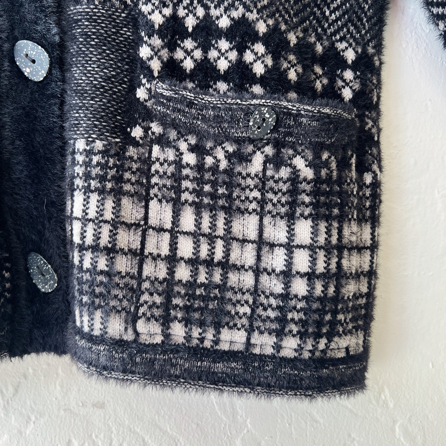 Close-up detail of Habitat Plaid Patchwork Cardigan showing button-flap hip pocket with speckled resin button, mixed plaid and Fair Isle knit panels in black and cream, and soft eyelash-textured nylon blend fabric
