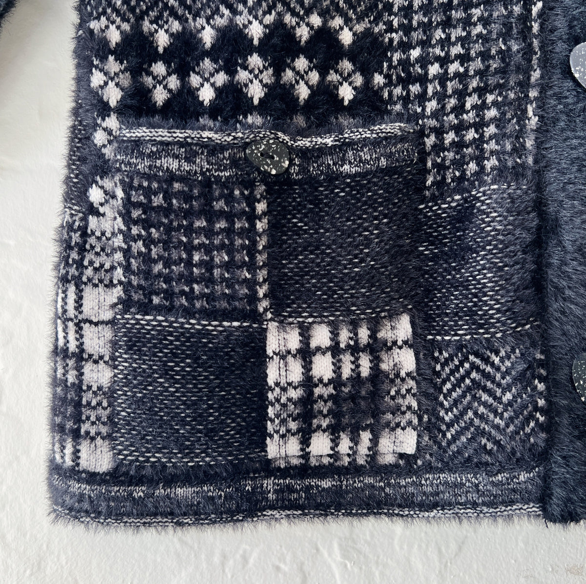 Close-up detail of Habitat Plaid Patchwork Cardigan showing mixed patchwork knit panels including windowpane plaid, houndstooth, and herringbone in black and cream with soft eyelash texture and button-flap pocket
