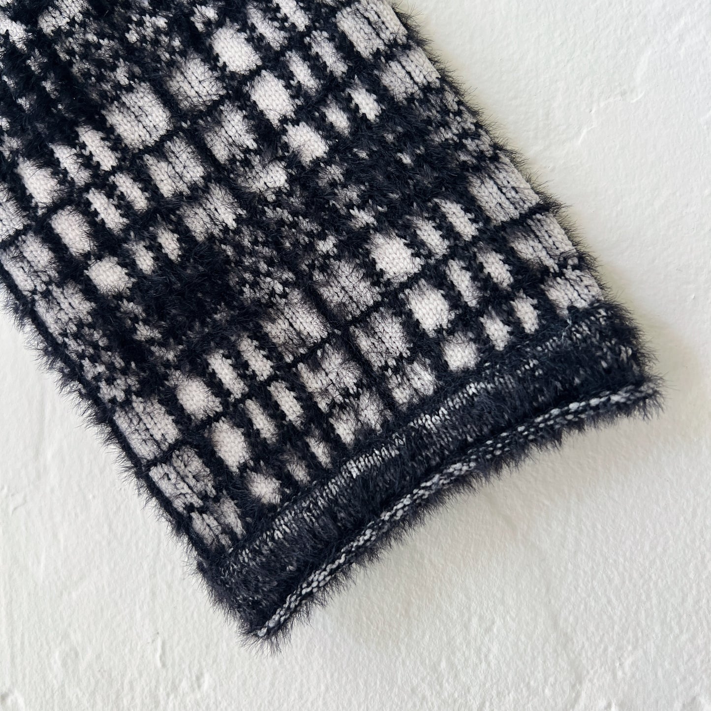 Close-up detail of Habitat Plaid Patchwork Cardigan sleeve and ribbed cuff showing windowpane plaid knit in black and cream with soft eyelash-textured nylon blend fabric and knitted hem trim
