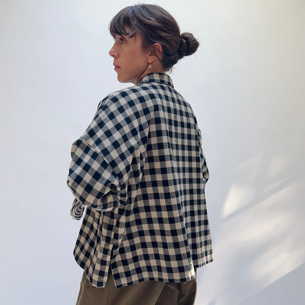 Model wearing the Eleven Stitch Big Check Big Shirt in Fennel, back view, showing relaxed boxy silhouette and side vents in black and tan gingham cotton

