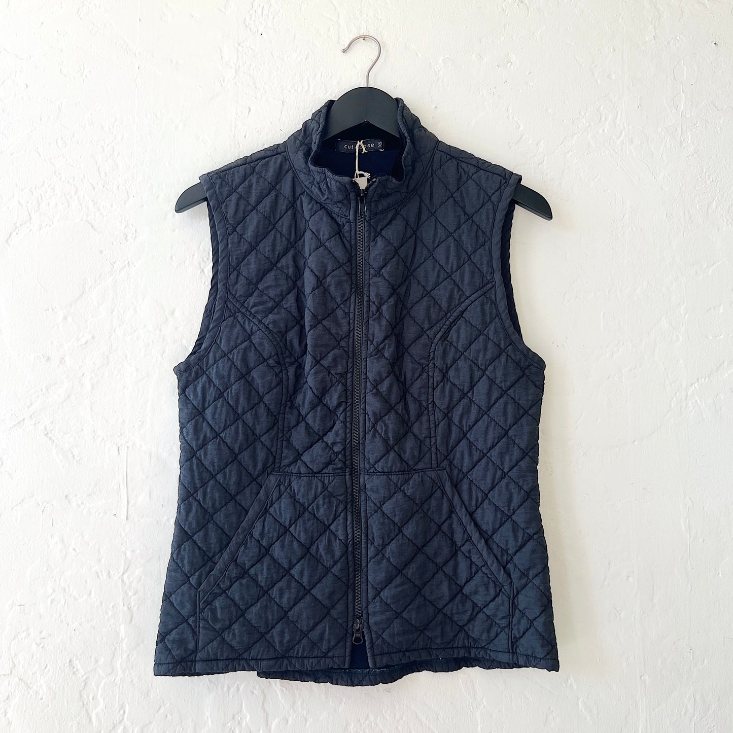 Navy quilted vest on a hanger against a white wall