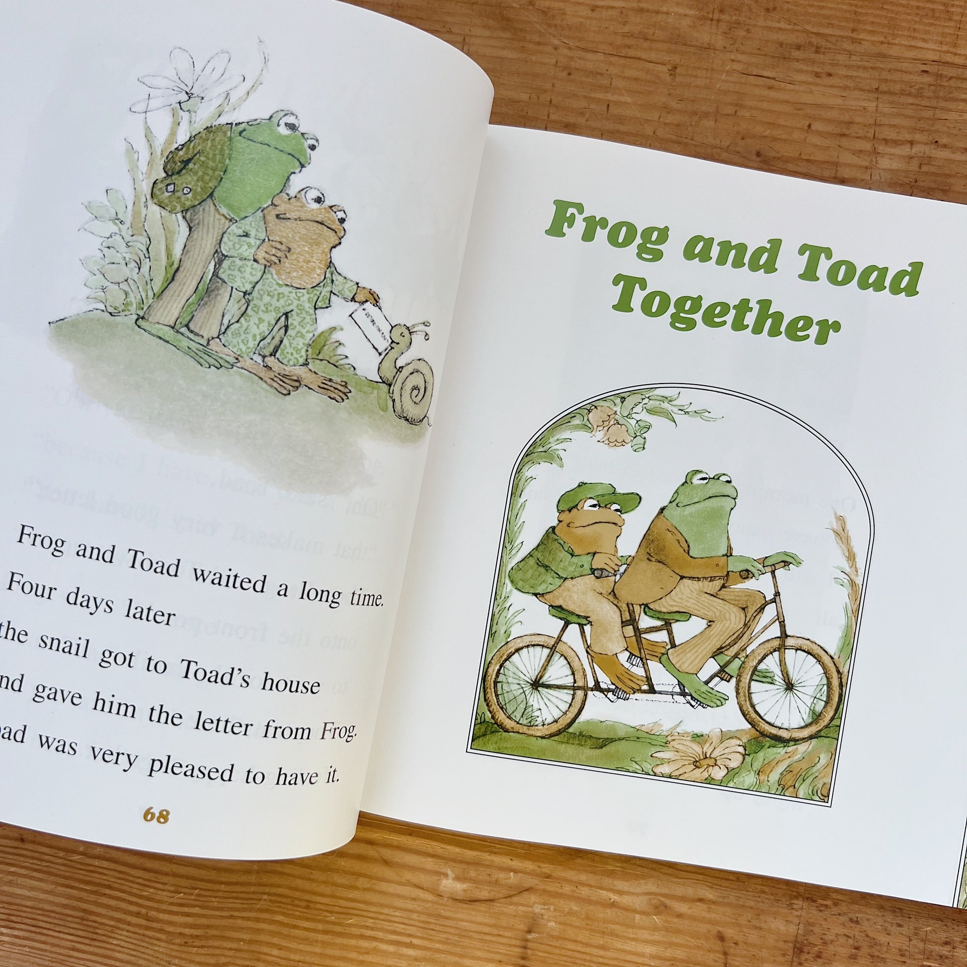 Open interior spread of Frog and Toad Storybook Favorites showing a page from Frog and Toad Are Friends with an illustration of Frog and Toad with a snail, and the title page of Frog and Toad Together with an illustration of Frog and Toad riding a tandem bicycle, displayed on a warm wood surface.
