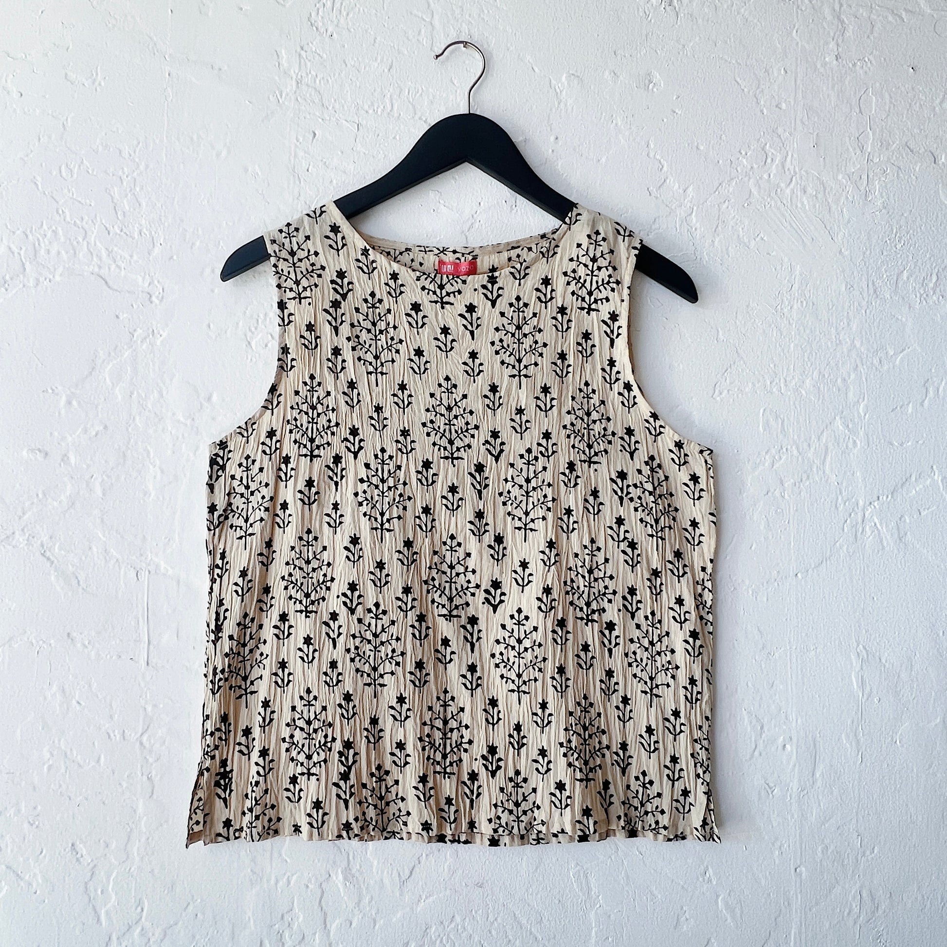 Beige sleeveless top with black floral pattern on a hanger against a white wall