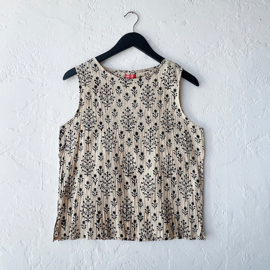 Beige sleeveless top with black floral pattern on a hanger against a white wall