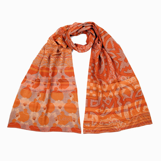 Létol Gisele Scarf in Orange, draped and loosely knotted against a white background, showing a reversible Jacquard-woven organic cotton scarf with warm tangerine and terracotta tones featuring large rounded geometric motifs on one side and an abstract architectural pattern on the other, with a woven Létol label visible at the border
