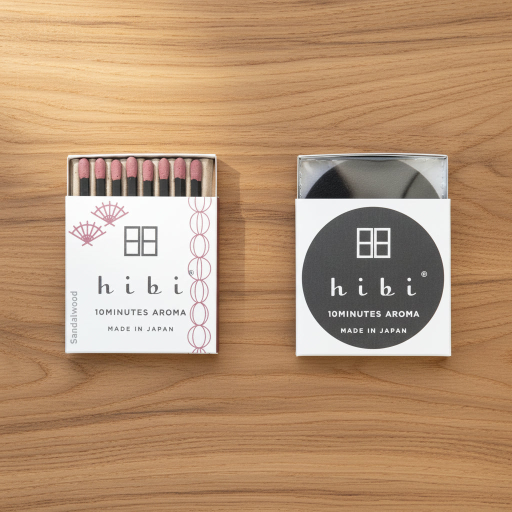 Two Hibi Sandalwood Incense Match boxes on a wood surface — one open showing 8 match-style incense sticks with dusty rose tips and a Japanese fan motif, 'Sandalwood' on the spine, one closed showing the Hibi 10 Minutes Aroma logo, Made in Japan
