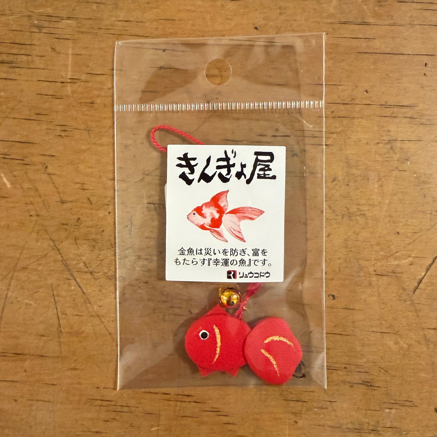 Red goldfish charm in clear packaging on a wooden surface