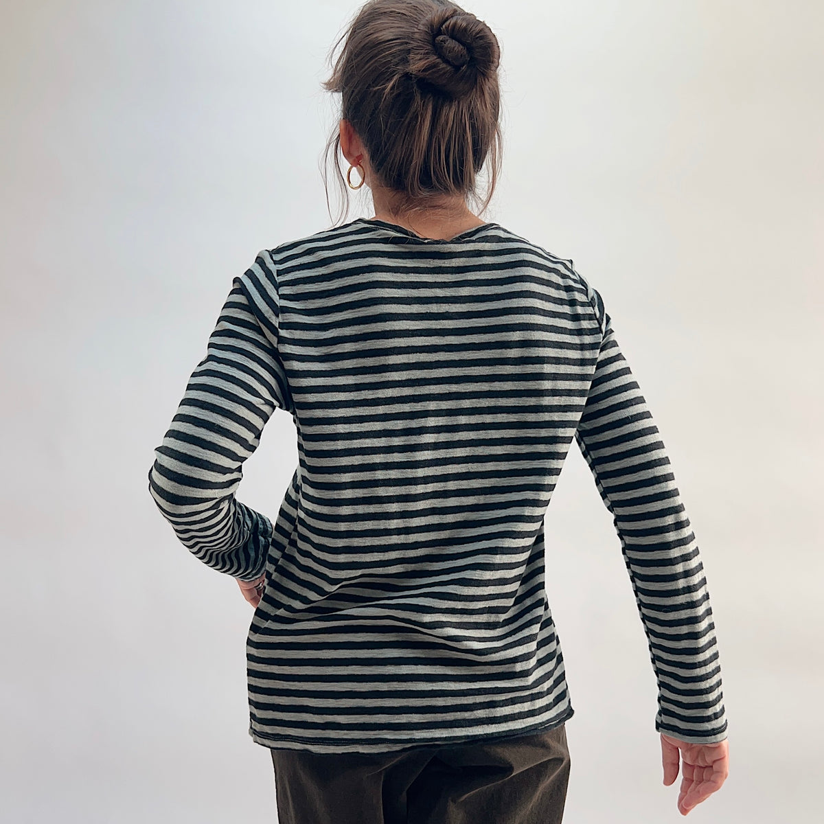 Cut Loose Striped Long Sleeve Easy Tee in Squirrel, black and grey stripe crewneck tee with hair in bun, worn with dark wide-leg trousers — back view showing seam detail and hem

