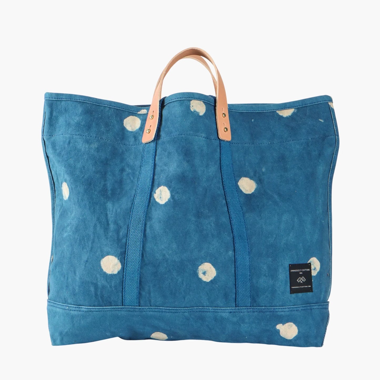 Blue tote bag with white floral patterns and brown handles on a white background