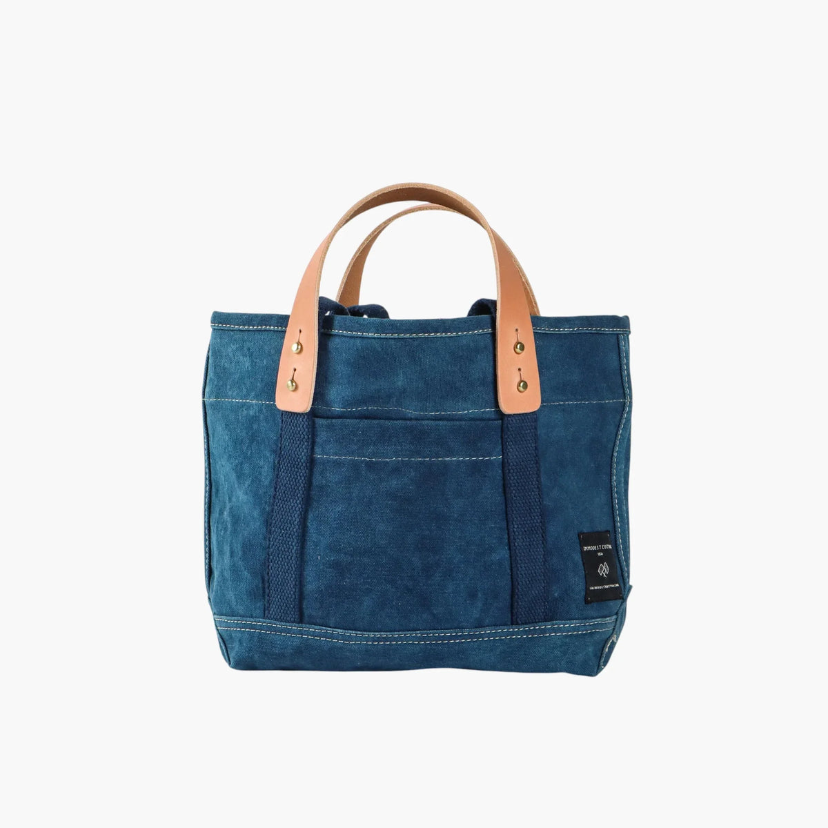 Immodest Cotton Lunch Tote in Indigo with natural leather handles, a front pocket, and contrast white stitching.
