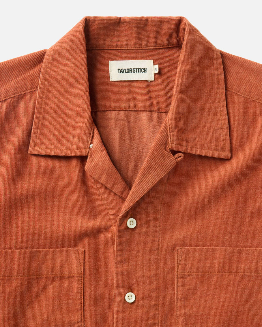 Close-up of Taylor Stitch Conrad Shirt in Heather Chili Pincord showing open camp collar detail, Taylor Stitch label, natural corozo button, and fine-wale pincord texture in warm heather chili organic cotton

