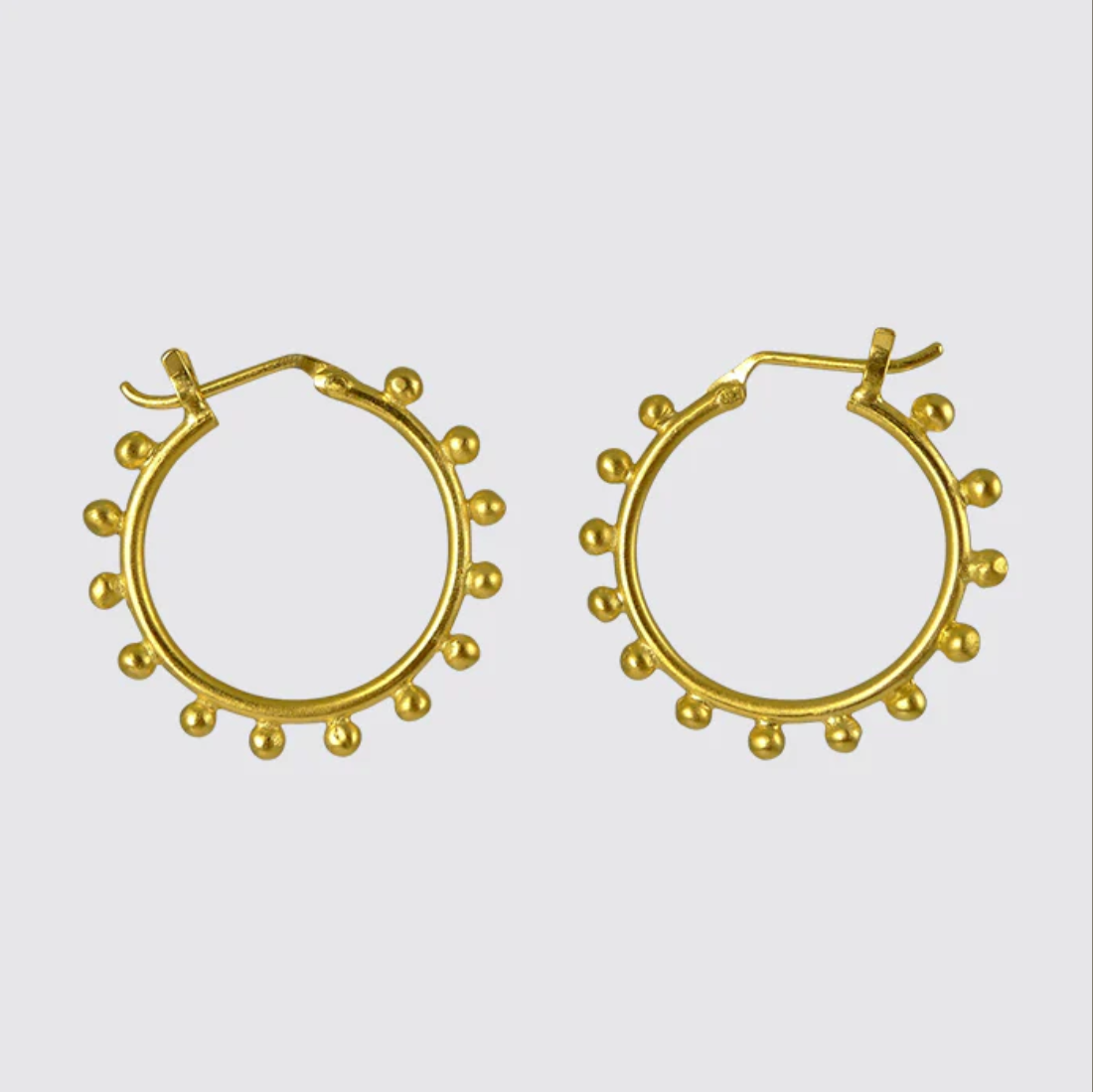 Gold hoop earrings with small spherical embellishments on a light gray background