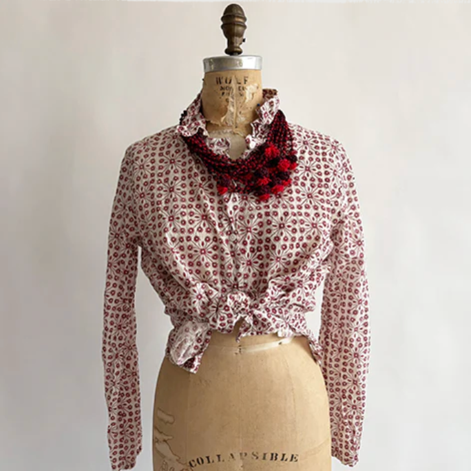 Mannequin wearing a patterned blouse with a red scarf on a plain background