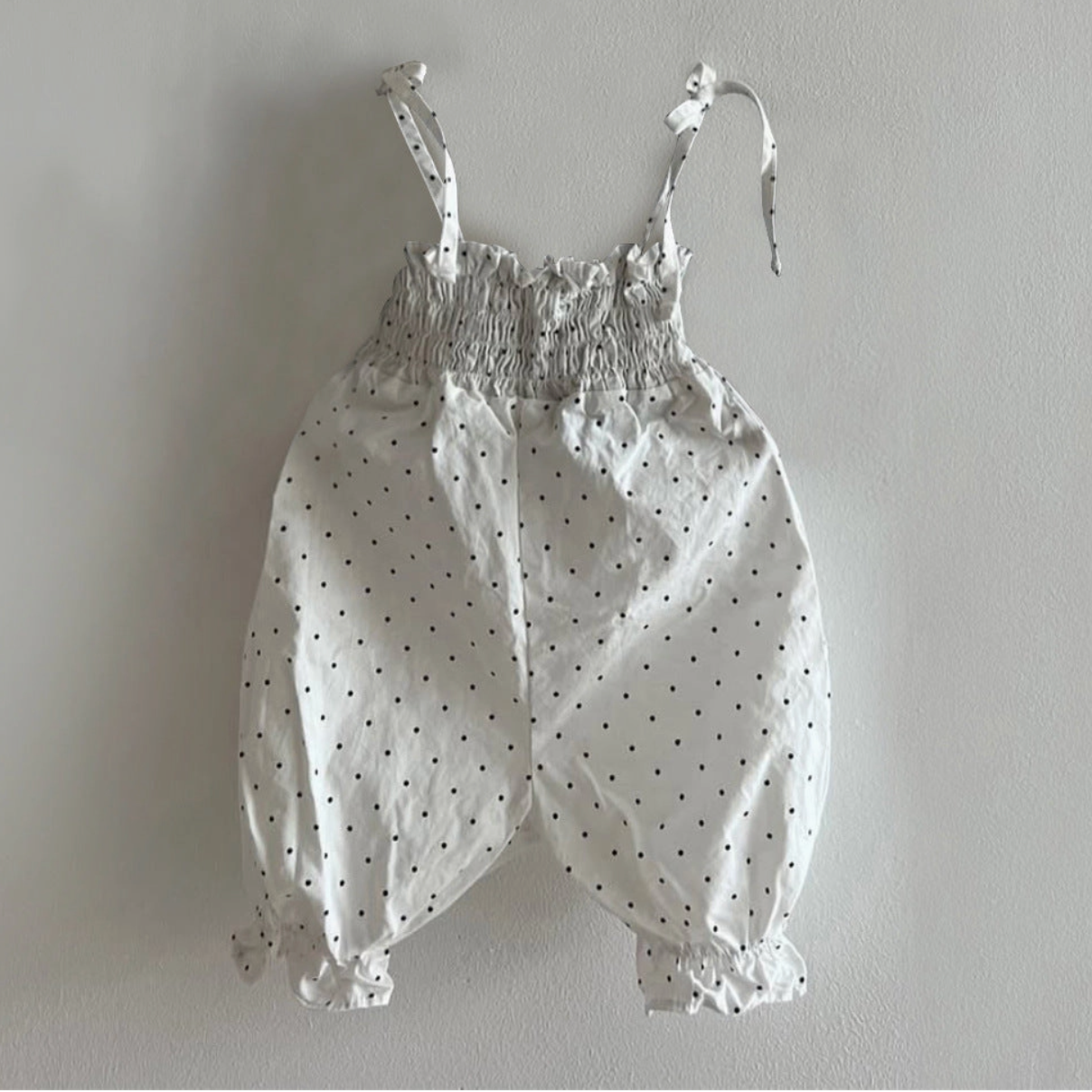 White baby romper with black polka dots on a gray background