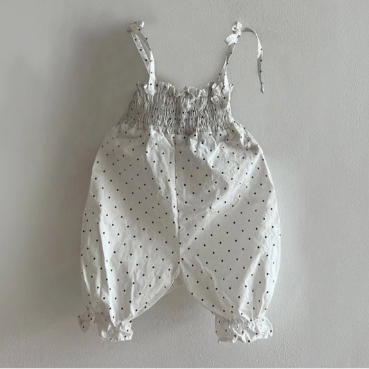 White baby romper with black polka dots on a gray background