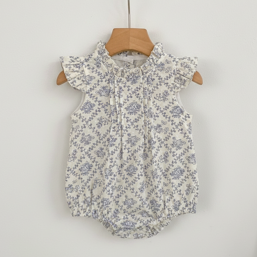 Floral baby romper on a hanger against a white wall with a wooden shelf in the background.