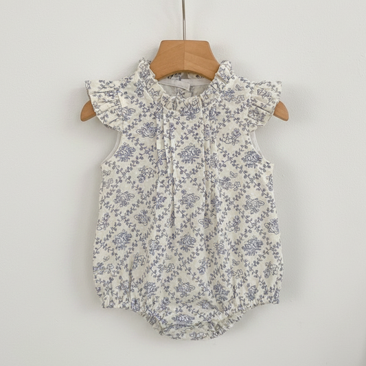 Floral baby romper on a hanger against a white wall with a wooden shelf in the background.