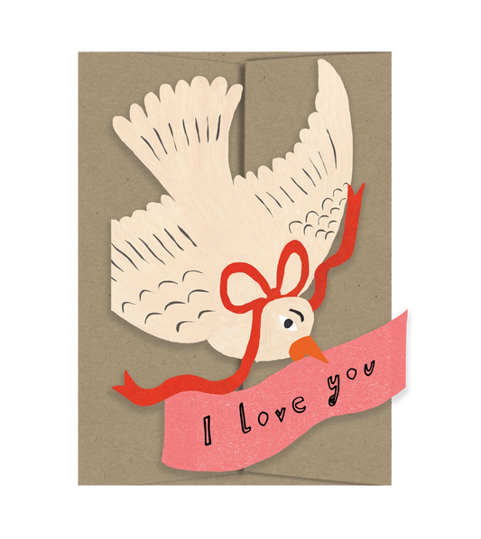 Isatopia Love You Bird Card, cream die-cut bird with outstretched wings and a red ribbon above a pink “I love you” banner, shown against a kraft envelope.
