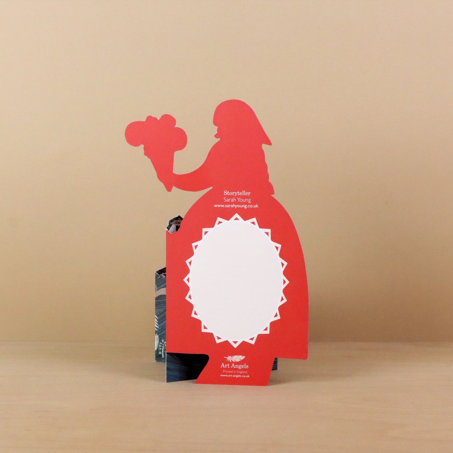 Reverse of the Storyteller die-cut concertina card showing a red silhouette of a woman holding flowers with a blank white message panel framed by a star-burst border, titled Storyteller by Sarah Young, printed by Art Angels
