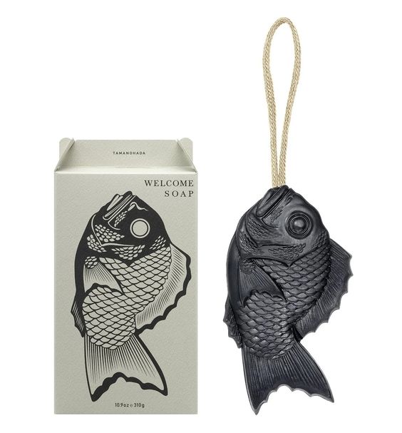 Tamanohada Muscovado Welcome Soap — deep charcoal bream fish-shaped soap on a natural linen rope, displayed beside its cream gift box printed with a bream fish illustration and 'Welcome Soap' text
