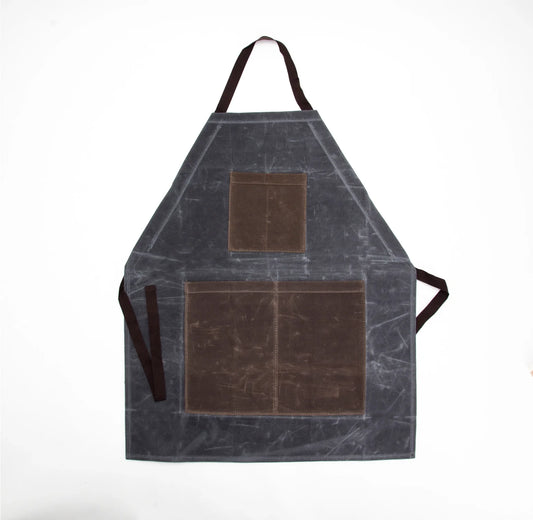 Slate gray waxed cotton apron with brown chest and divided lower pockets, a dark neck strap, and waist ties.
