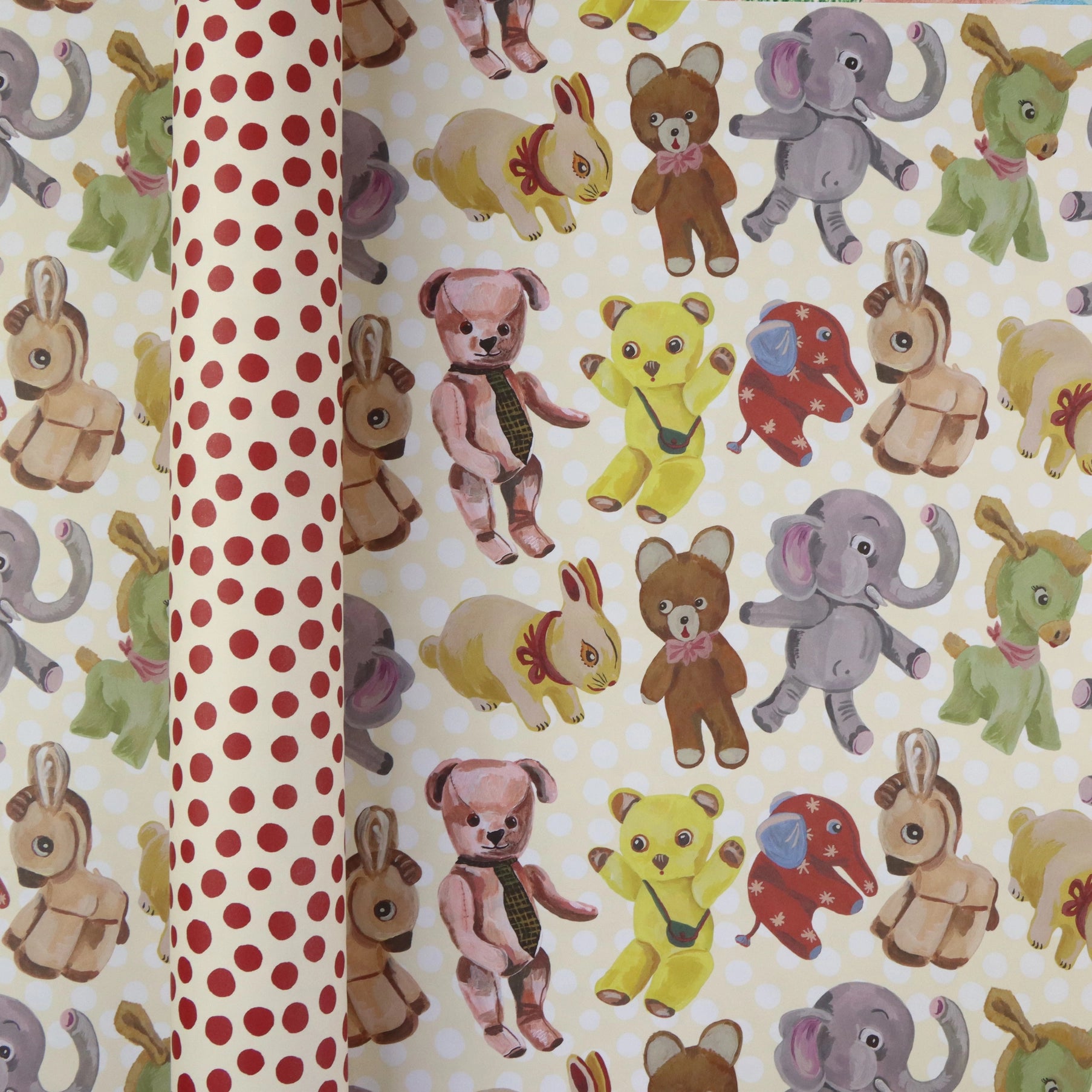  Plushies wrapping paper by Nathalie Lété shown rolled and flat, displaying vintage-style illustrated plush animals including teddy bears, elephants, rabbits, and donkeys on a cream background, with the red polka dot reverse visible on the rolled tube