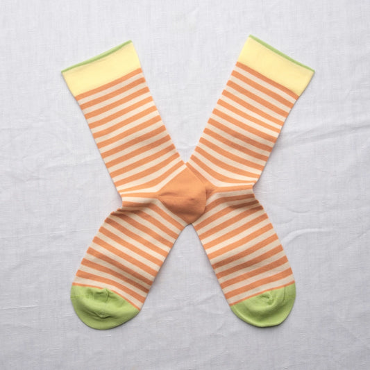 Adobe Striped Peach socks by Bonne Maison — fine horizontal peach and cream stripe cotton crew with yellow cuff and lime green heel and toe, flat lay pair crossed on a white linen background
