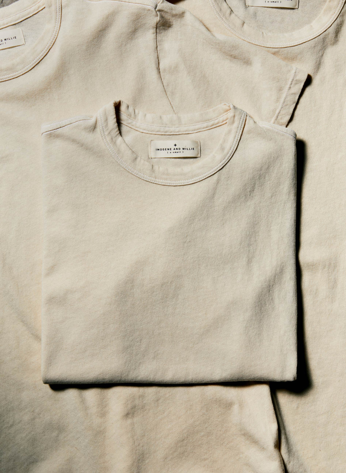 Three folded Imogene + Willie Classic Knit Midweight Crew t-shirts in Vintage White stacked together, Imogene and Willie label visible on top shirt — detail shot
