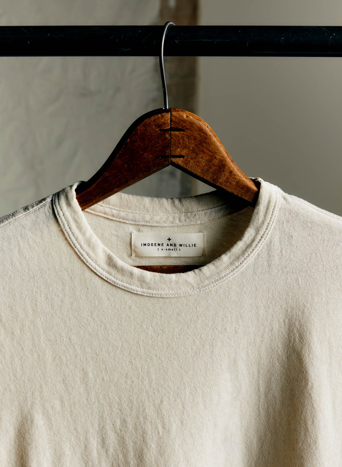 Close-up of the neckline and Imogene and Willie label on the Classic Knit Midweight Crew in Vintage White, hanging on a wooden hanger — label detail shot
