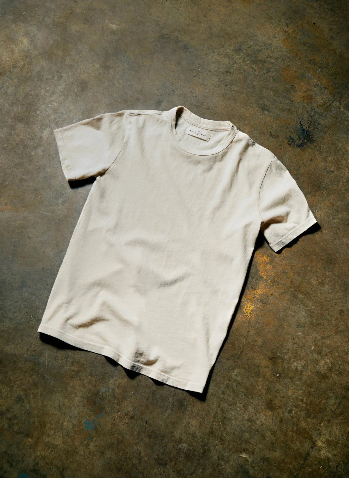 Imogene + Willie Classic Knit Midweight Crew in Vintage White, short-sleeve crewneck t-shirt laid on a concrete floor — overhead lifestyle shot
