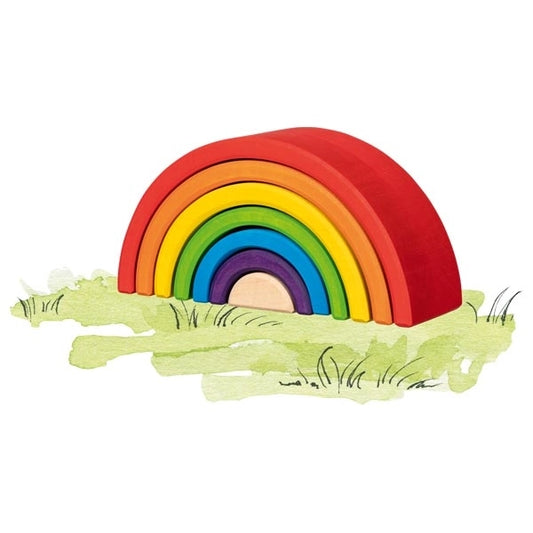 Goki Little Rainbow Building Blocks assembled as a classic rainbow arch on a watercolor grass illustration, showing 7 nested maple wood arches in red, orange, yellow, green, blue, purple, and natural wood from largest to smallest