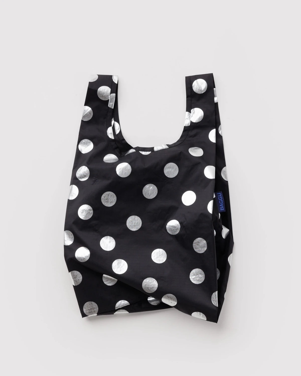 BAGGU Baby Baggu in Metallic Silver Polka Dot, shown unfolded with two handles and shiny silver dots on black fabric.
