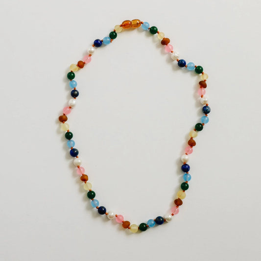 CanyonLeaf Raw Baltic Amber and Pearl + Multi Colored Gemstones Necklace — a hand-knotted necklace alternating raw honey amber, white pearl, pink rose quartz, blue aquamarine, navy lapis, green jade, and yellow amber beads with a honey amber screw clasp, laid flat on a light grey background