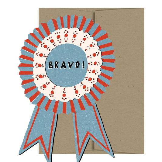 Isatopia Bravo Medallion Die Cut Card, blue-and-red award ribbon with a cream decorative ring and black “BRAVO!” lettering, shown against a kraft envelope.

